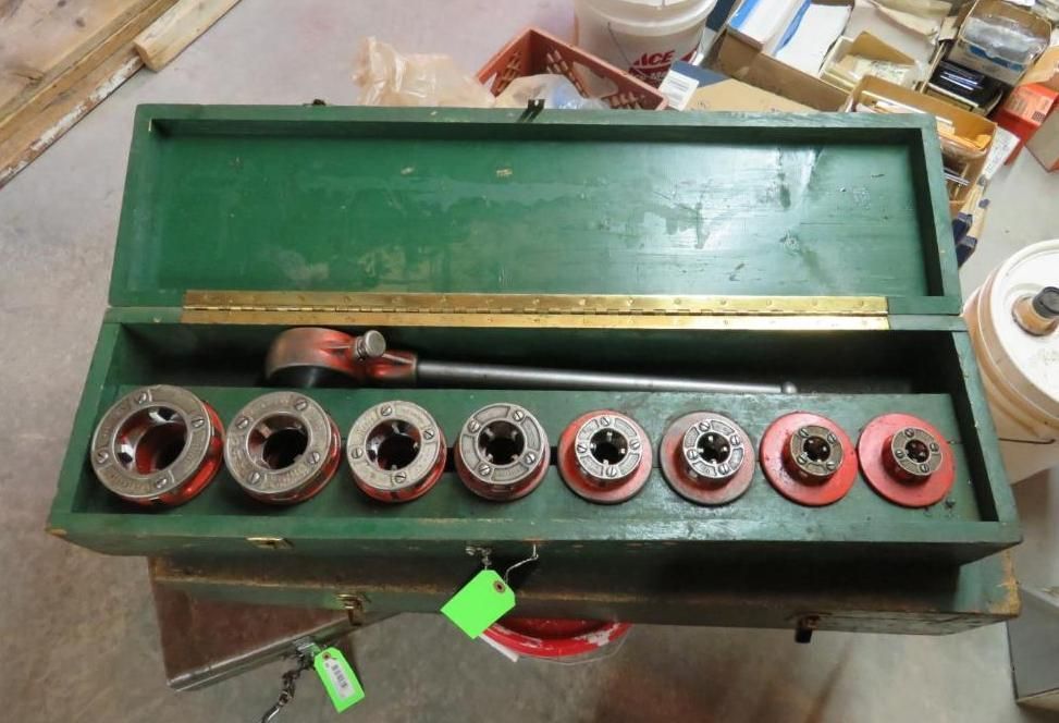 A green tool box open, containing pipe threader set and a ruler.