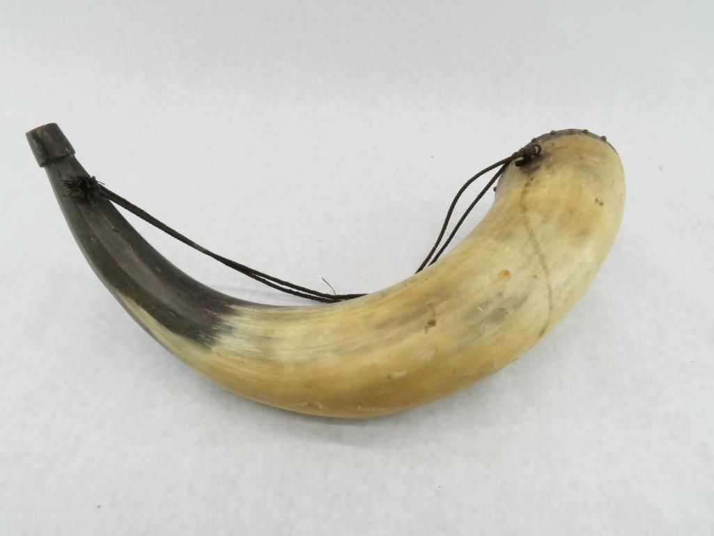 Powder horn with a black strap, curved, pale yellow and brown.