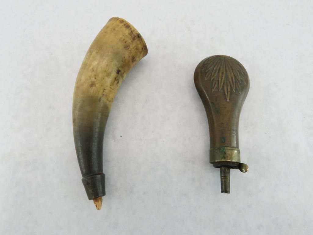 Powder horn and priming flask on white. Horn is light and dark brown. Flask is metal, brown.