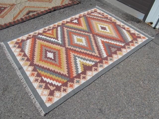 Rectangular rug with geometric diamond pattern in warm colors on asphalt.