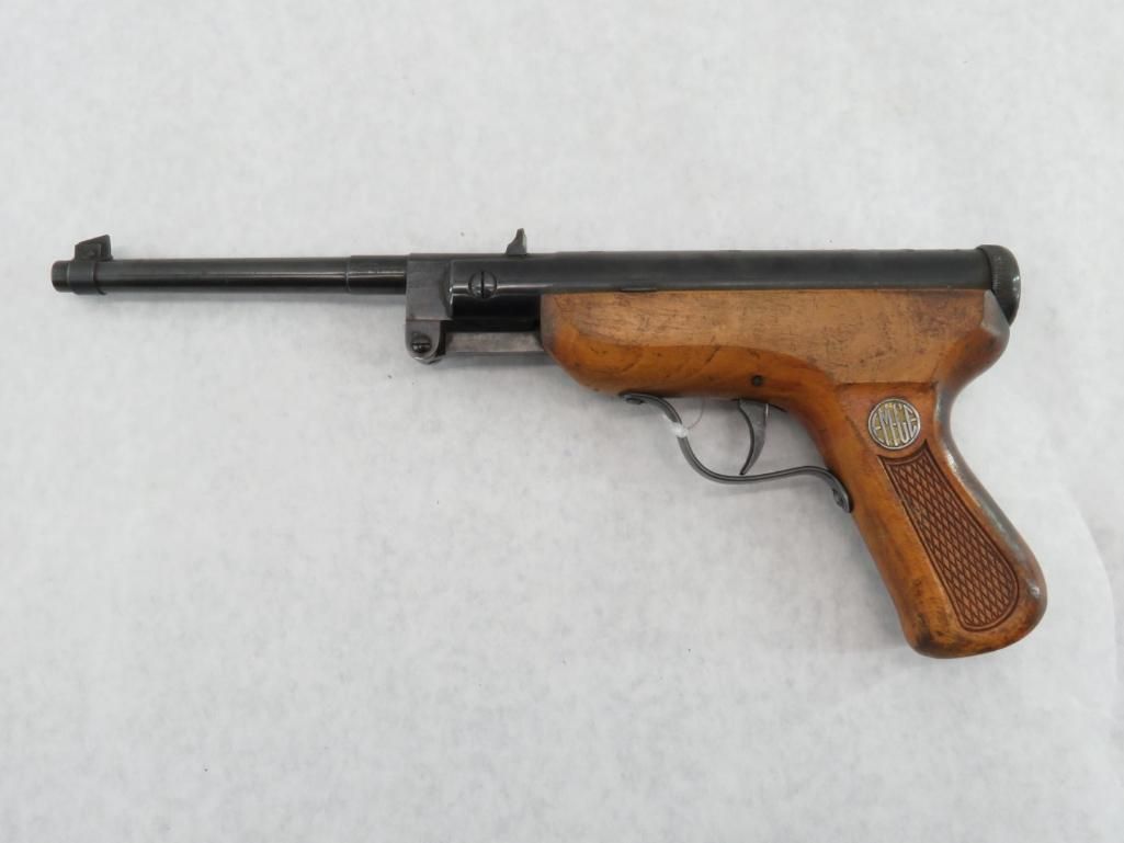 Air pistol with wooden handle, black barrel, and silver trigger, lying on a white surface.