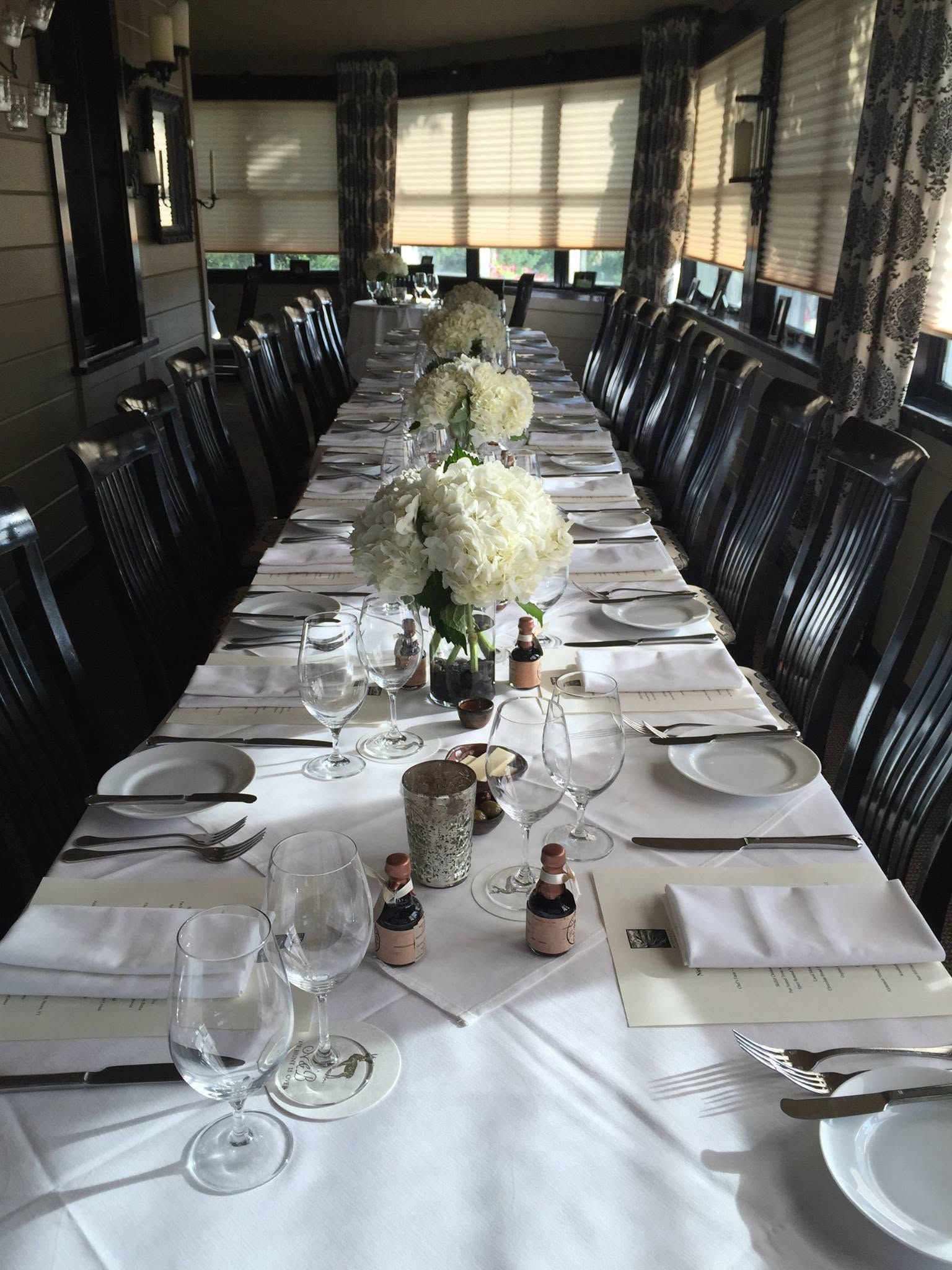 Long banquet table set with white linens, glassware, and floral centerpieces in a formal dining room