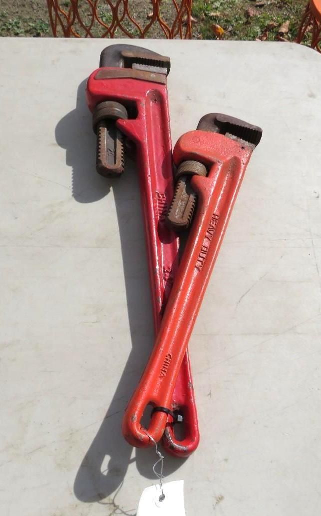 Two red pipe wrenches on a light-colored surface, one on top of the other.