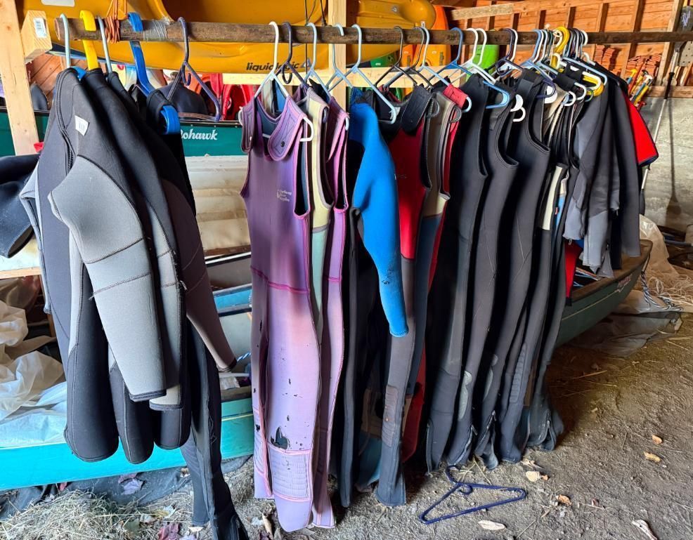 Wetsuits hanging on a rack in a wooden shed. Various colors.