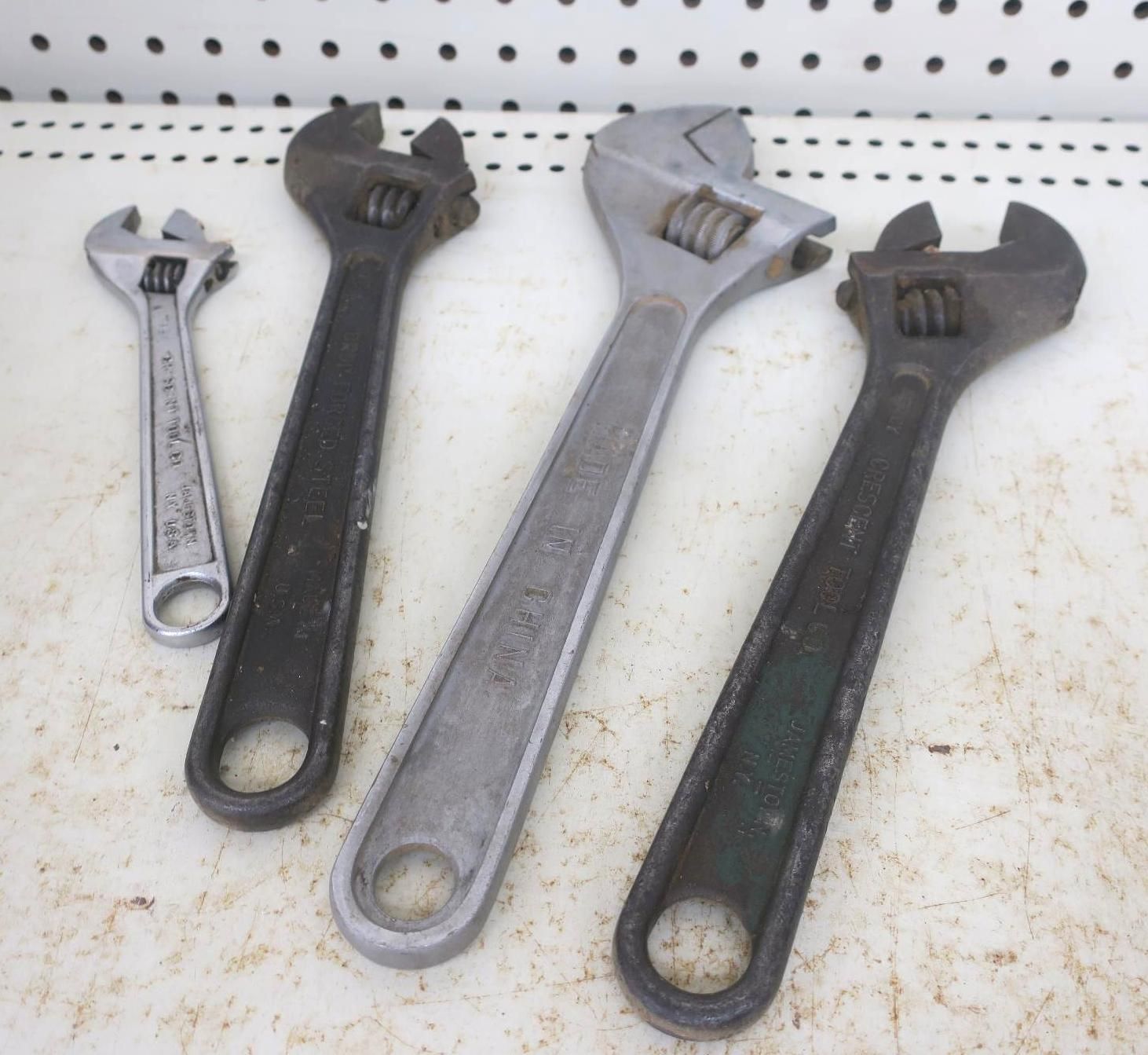 Four adjustable wrenches of different sizes laid on a white pegboard surface.