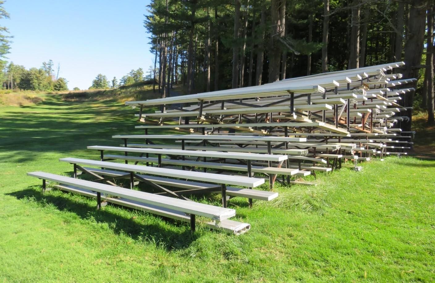 Bleacher seating on green grass, near trees. Sunny day.