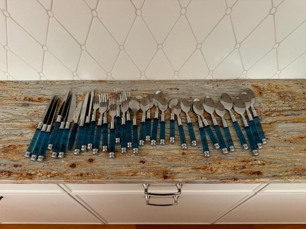 Silverware set with blue handles on a wooden-like surface, inside a case.