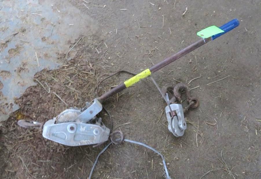 A come-along tool and pulley system on ground. Tool has handle, and metal cable.