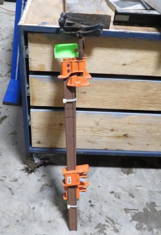Clamp with orange clamps on a brown bar, in front of a wooden cabinet.