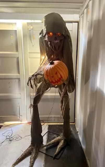 Animated Halloween figure holding jack-o'-lantern with glowing eyes, tall, spindly body.