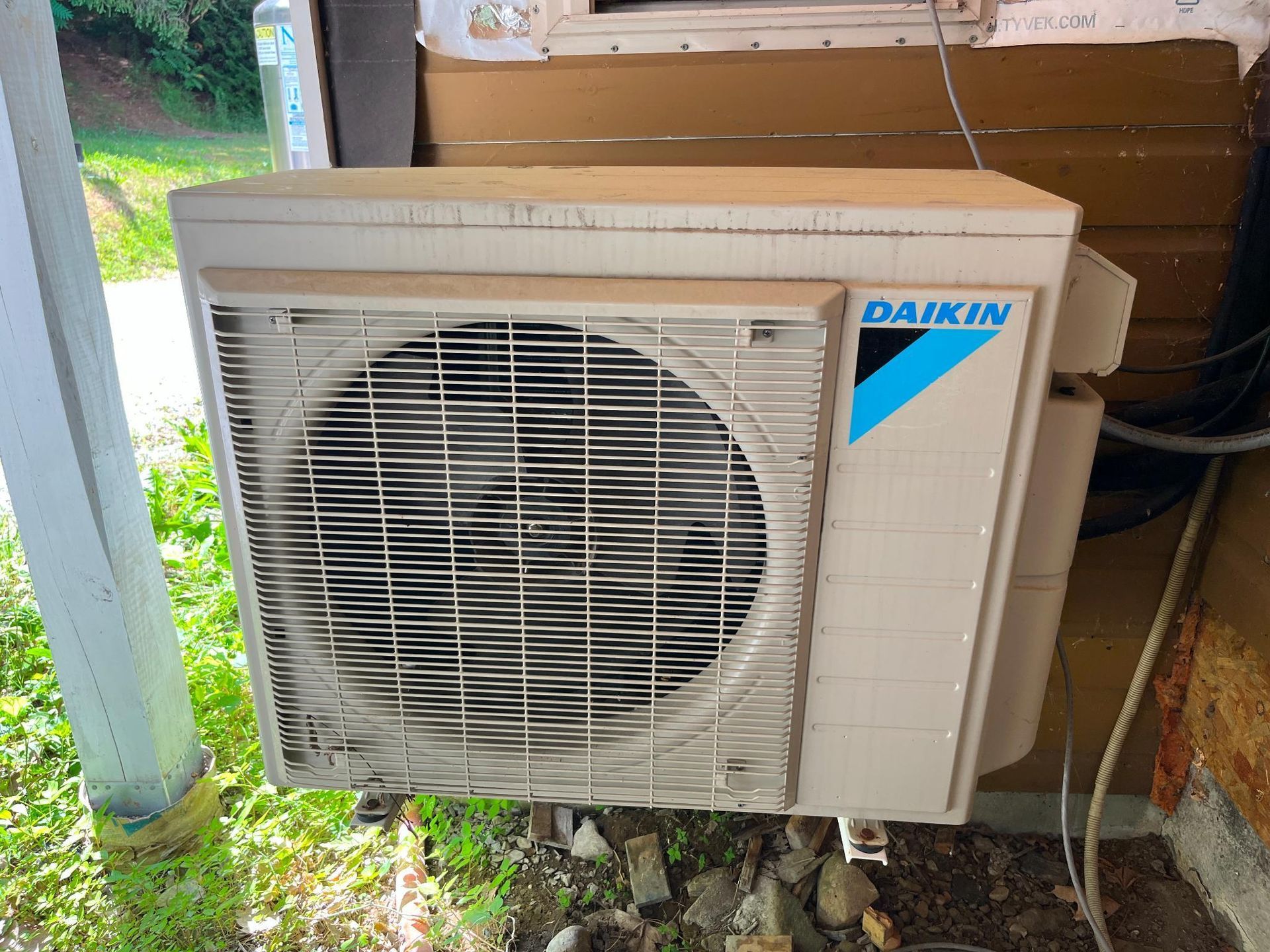 Daikin outdoor air conditioning unit against a wall with a beige and blue logo.