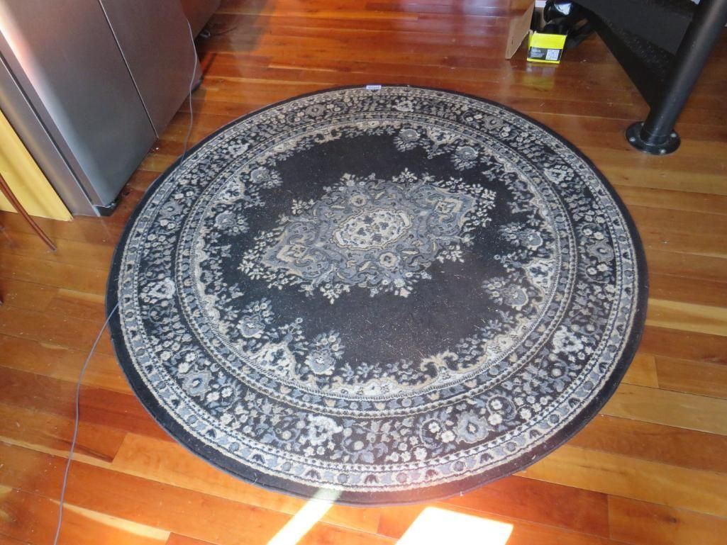 Round black rug with ornate floral design on a wooden floor.