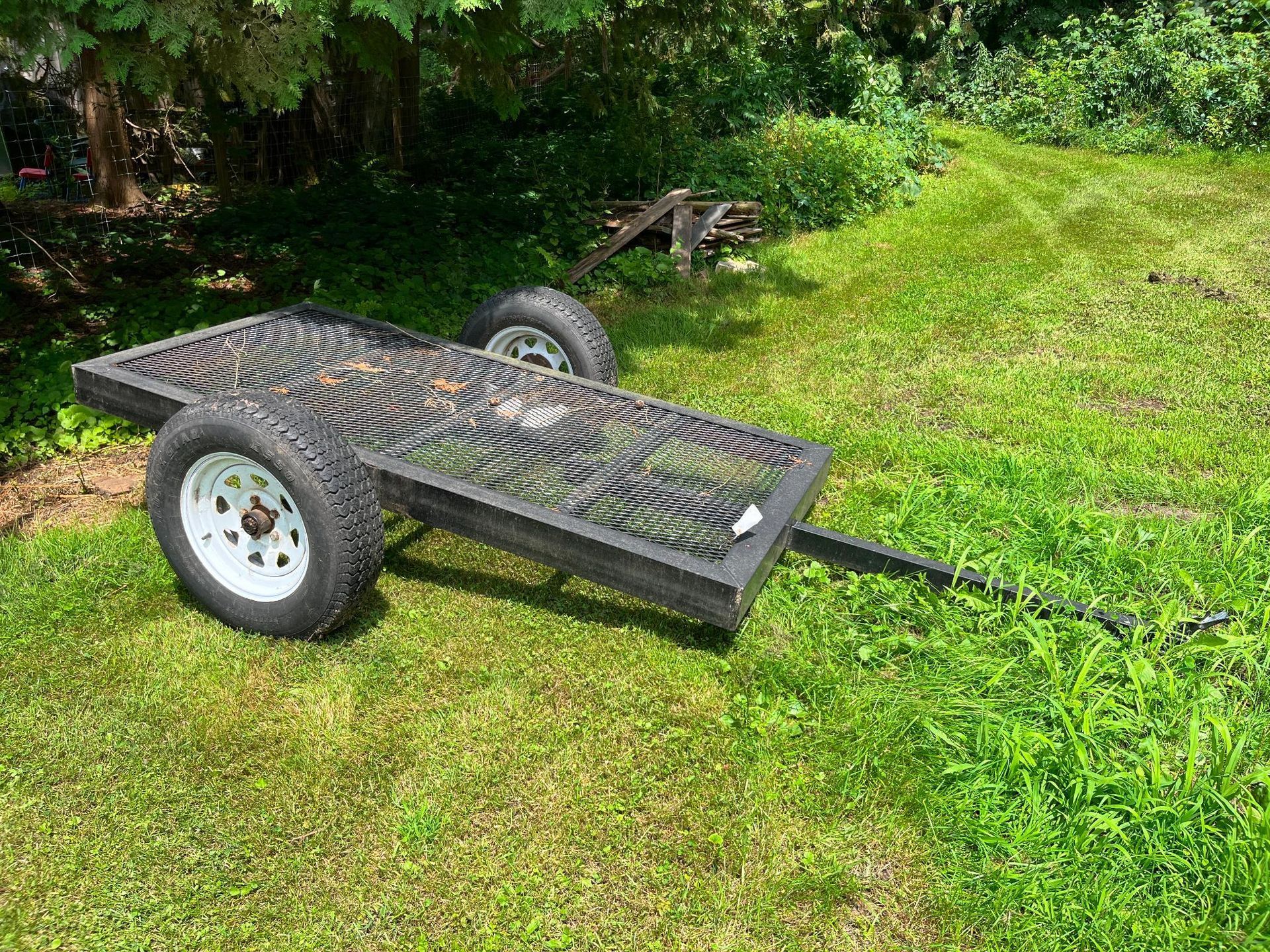 Black utility trailer with a patterned bed on grass.