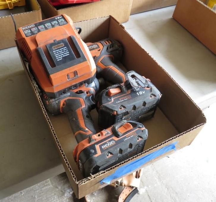 Cardboard box holding orange and black power tools, including drills and batteries.
