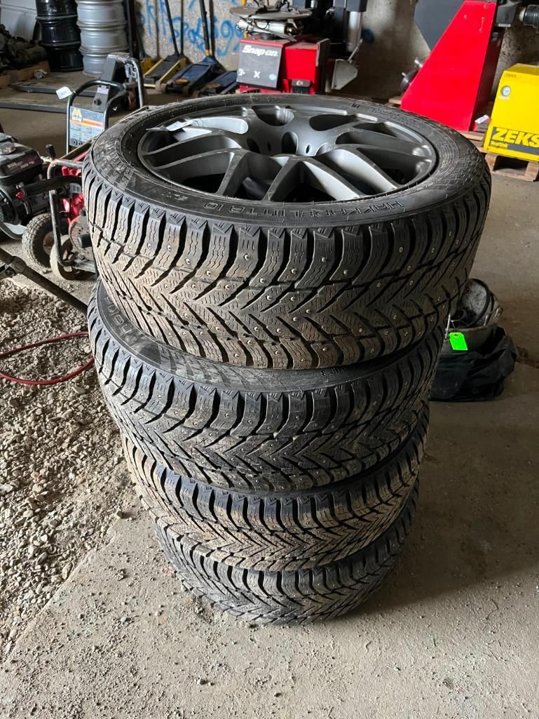 Four stacked tires with alloy wheels; indoor setting.