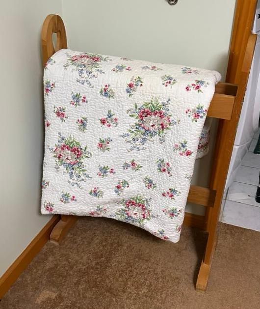 Quilt with floral pattern draped over a wooden quilt rack in a room.