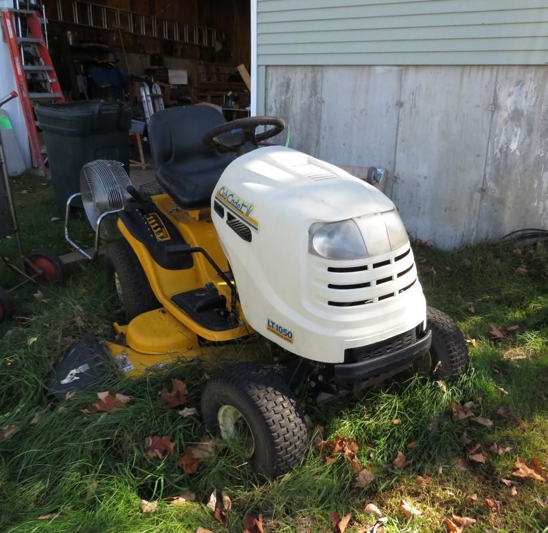 Yellow Cub Cadet riding lawnmower parked on grass next to a building.