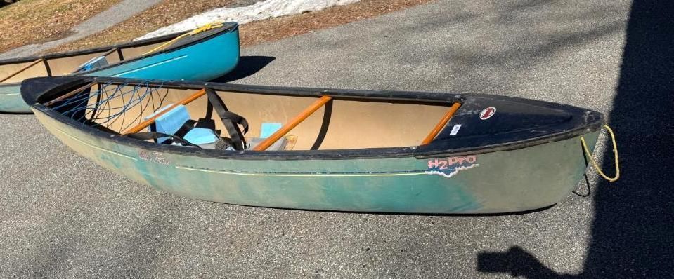 A green canoe with a black rim is on a paved surface. 