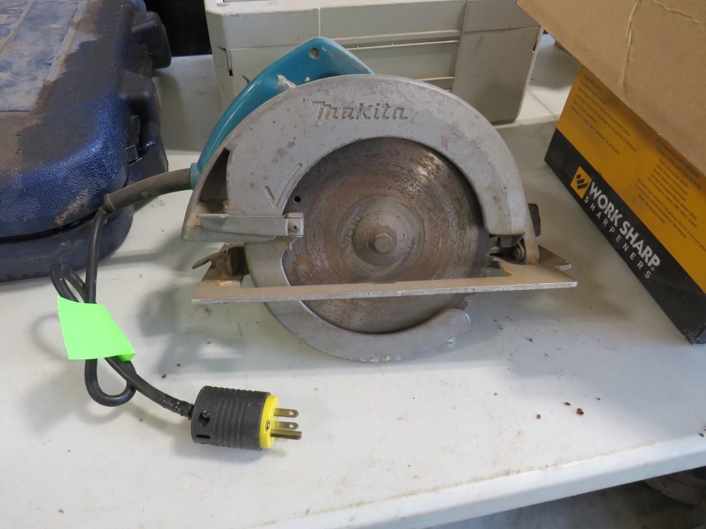 A Makita circular saw with a cord and a plugged-in end. The saw is on a white surface.