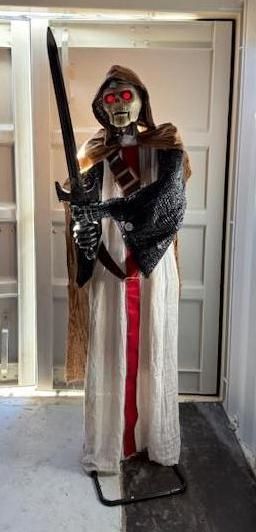 A Halloween decoration of a hooded skeleton knight holding a sword. It has glowing red eyes and is standing.
