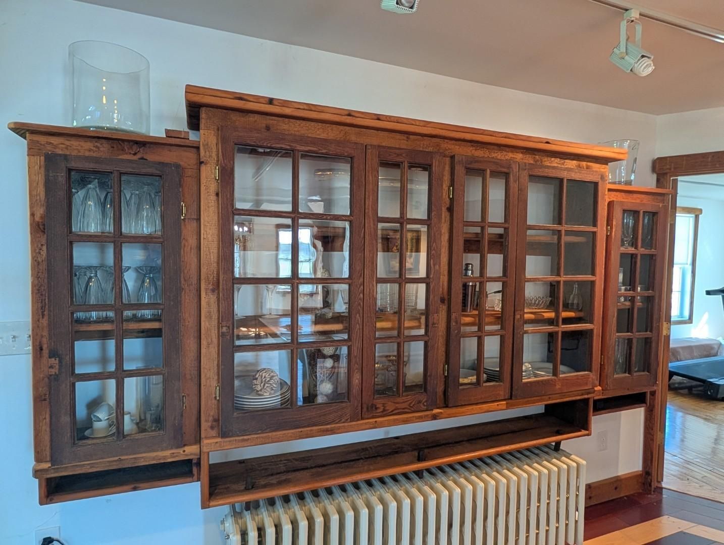 Large wooden wall cabinet with glass doors above a radiator in a bright room