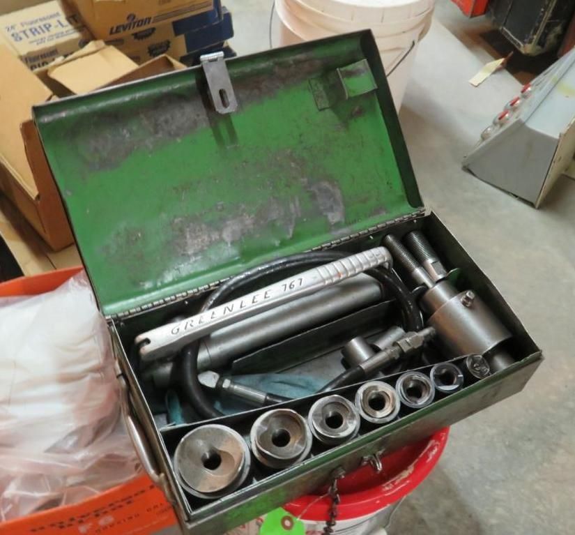 Open green metal tool box with tools, including punches and a hydraulic ram.