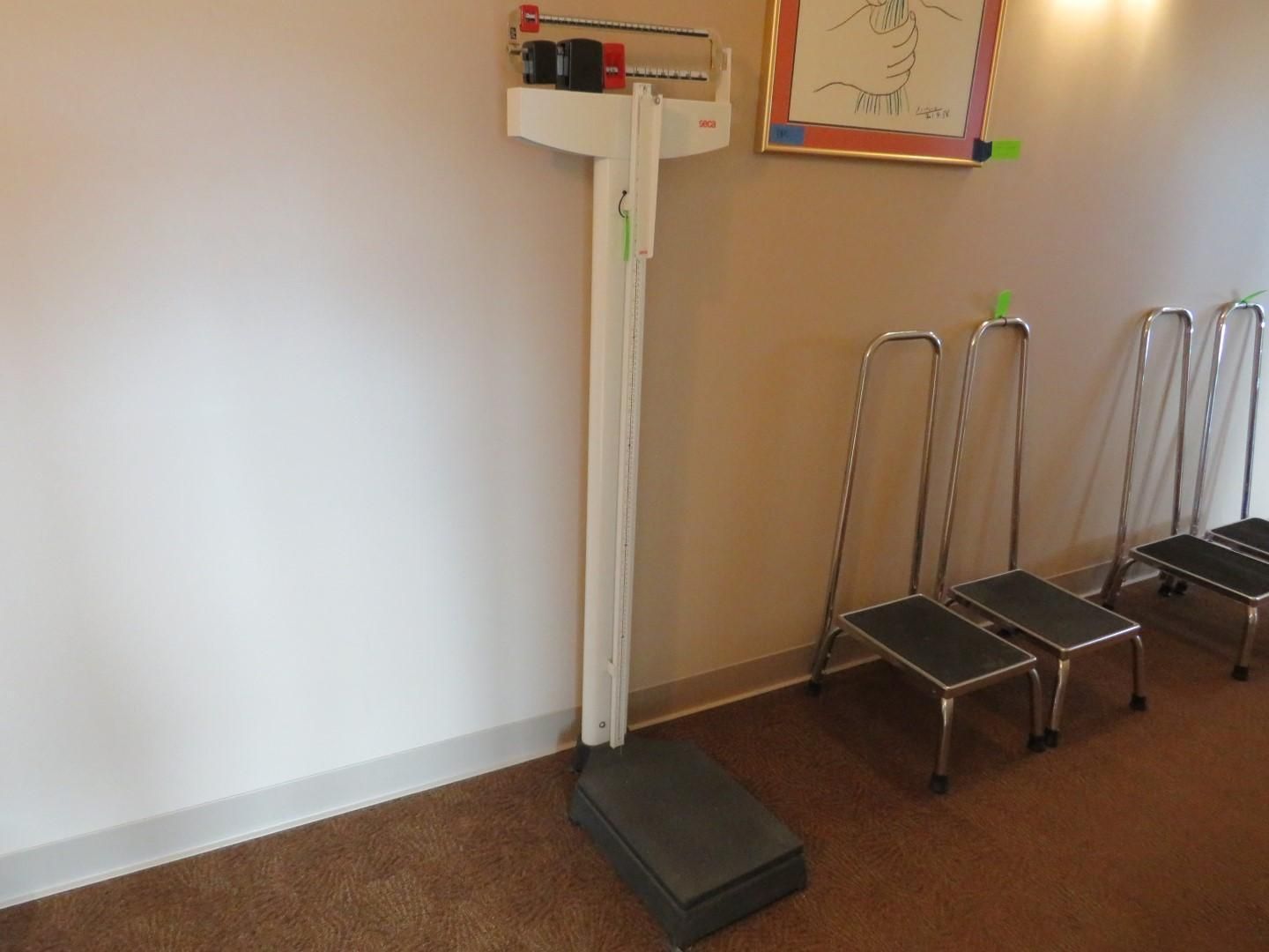 Medical scale and three step stools near a wall.