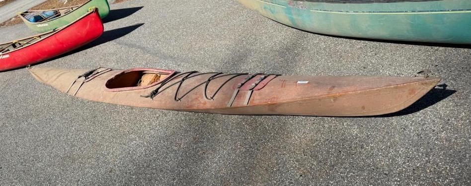 Brown kayak on asphalt with red and green canoes in background.