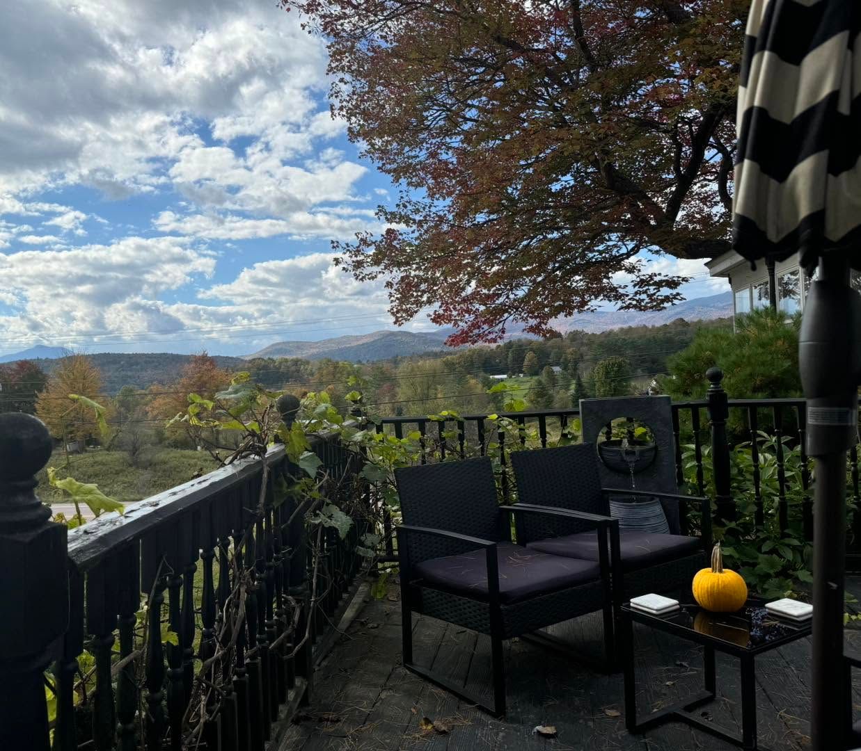 Patio with black chairs, small table and pumpkin overlooking a wooded valley under a cloudy sky