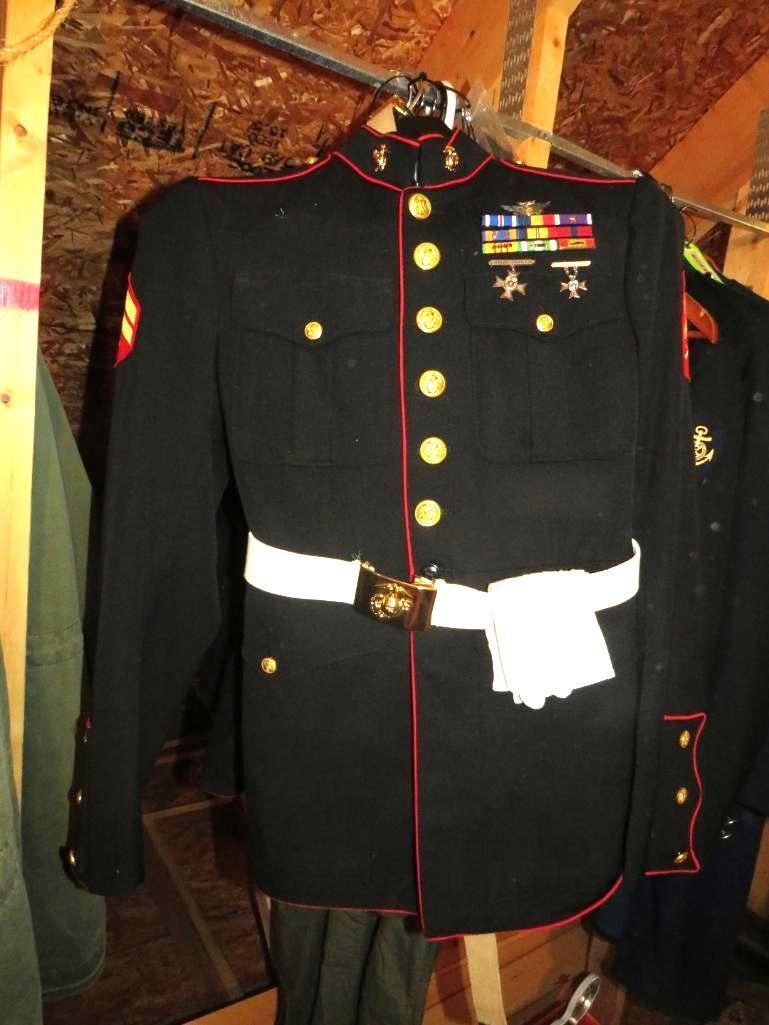 Marine Corps dress blue uniform on a hanger, white belt, gold buttons, ribbons, red trim, dark setting.