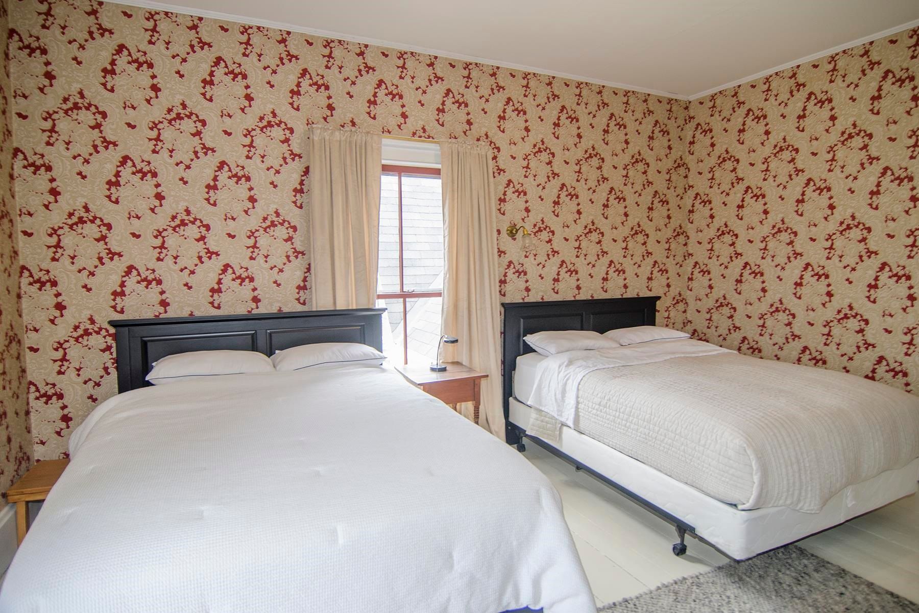 Two beds in a room with patterned wallpaper, curtains, and a window.