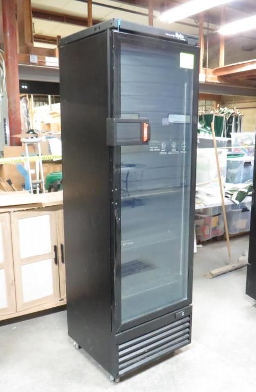 Black commercial refrigerator with glass door in a workshop setting.