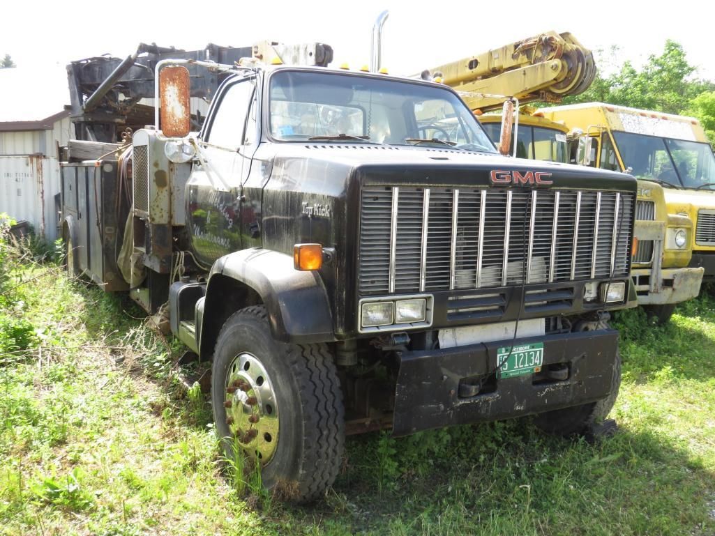 Black GMC truck with crane equipment, parked on grass near a shed and yellow vehicle.
