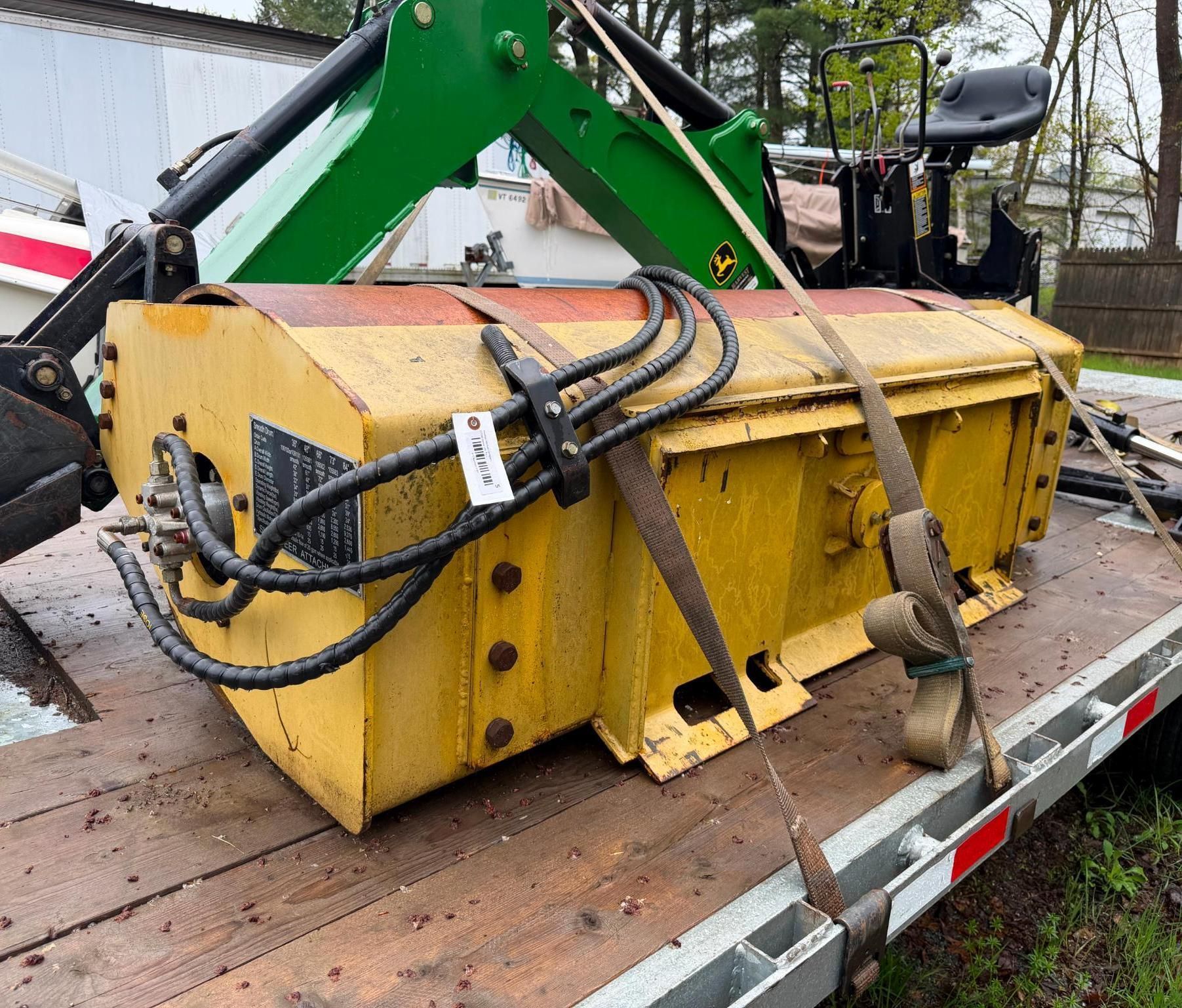 Yellow industrial machine attachment strapped on a flatbed trailer next to a green excavator arm.