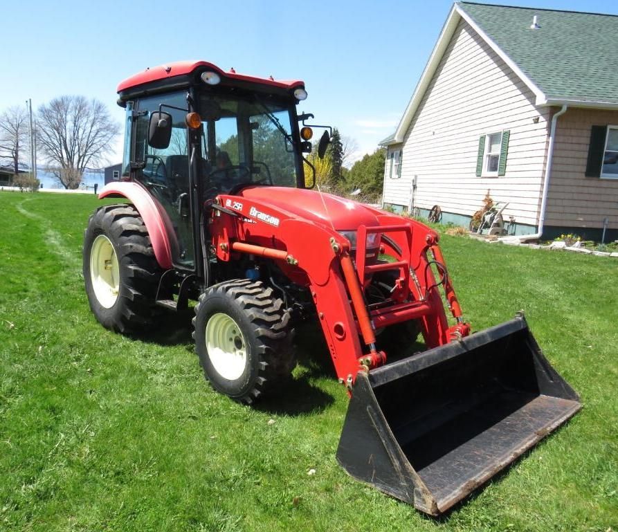 Red tractor with front loader on a grassy lawn next to a house.