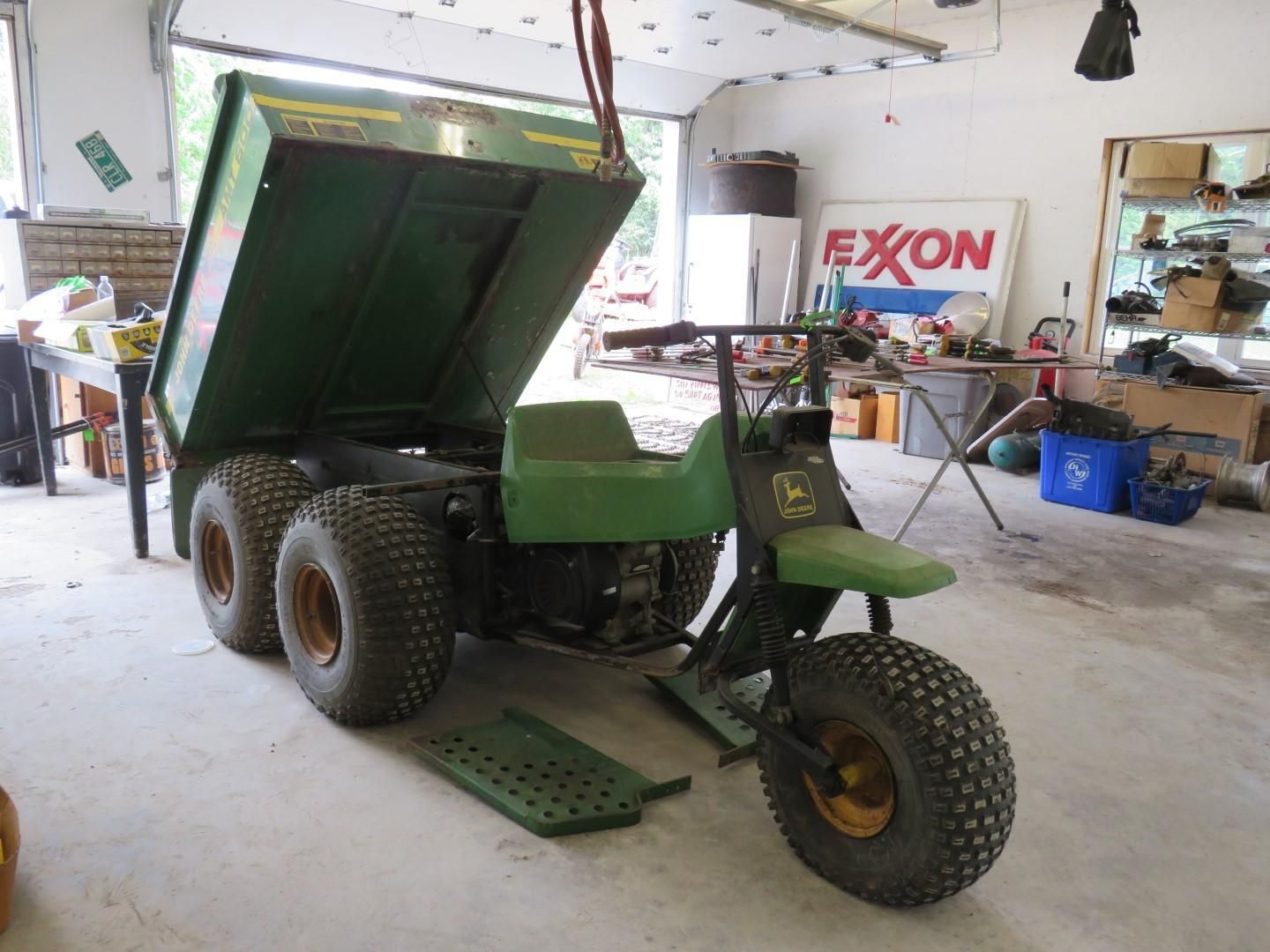 Green John Deere six-wheeled dump tricycle inside a garage with its bed raised.