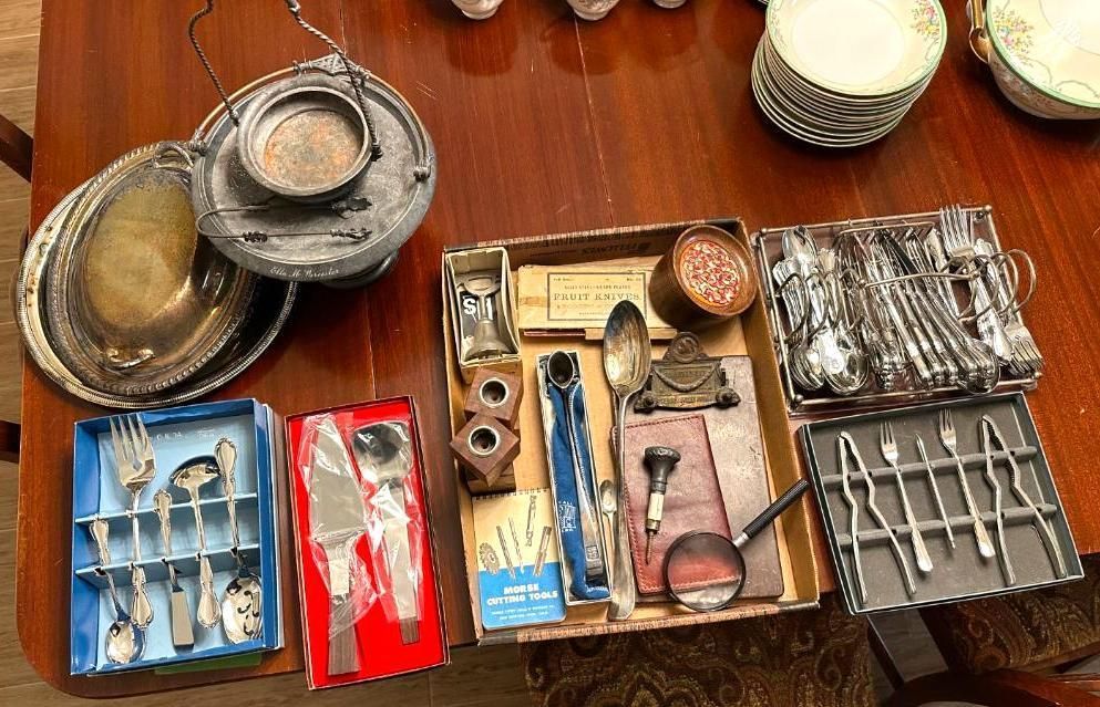 A table with antique silverware, serving dishes, and storage boxes.