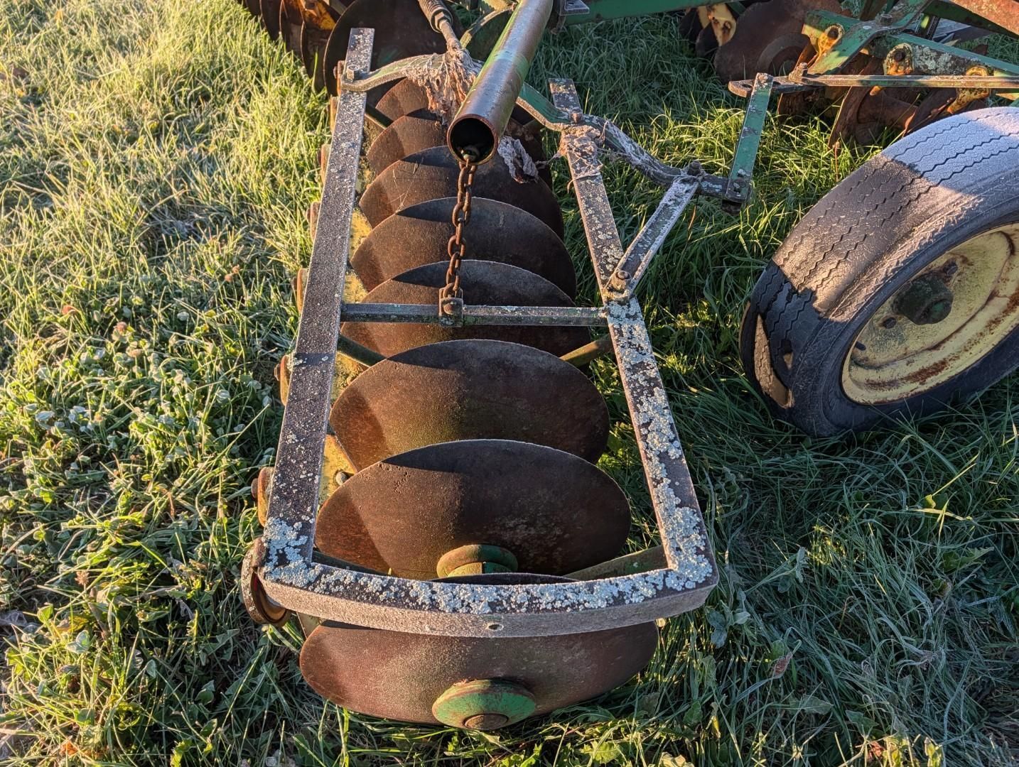 antique metal auger drill on grass beside a wheelbarrow tire