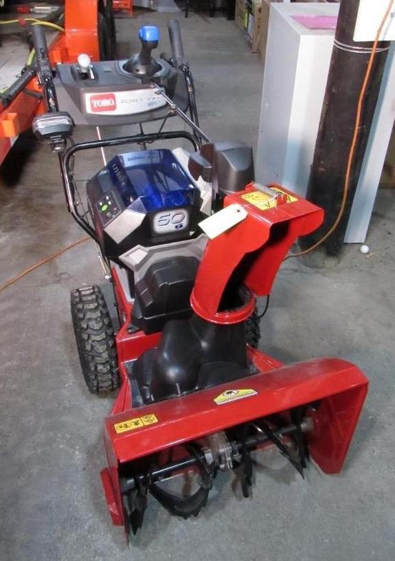 Red and black Toro snowblower with a blue engine, on a gray floor.