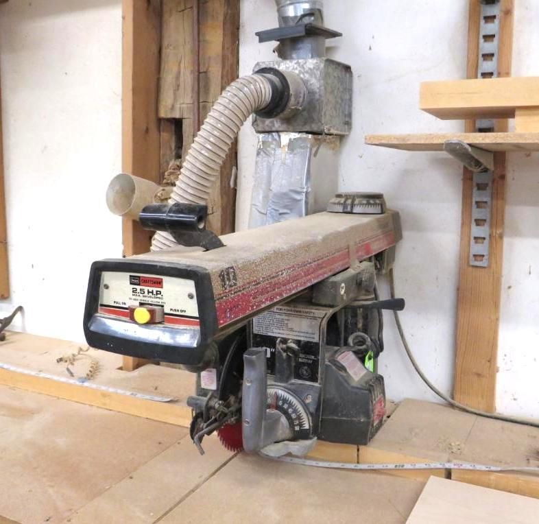 A radial arm saw, mounted on a workbench, with dust collection system attached.
