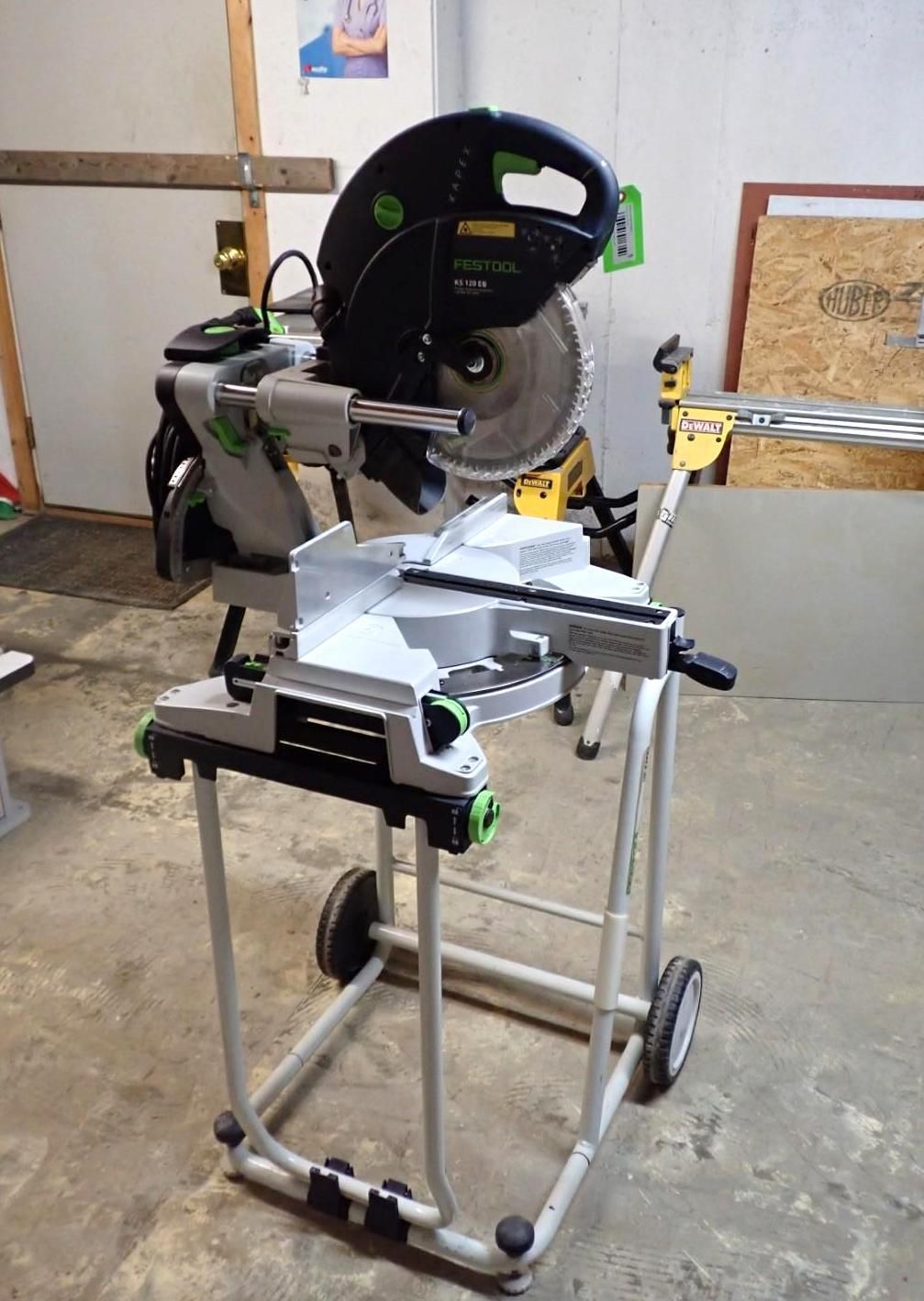 Festool miter saw on a wheeled stand. Gray, black, and green, in a workshop setting.