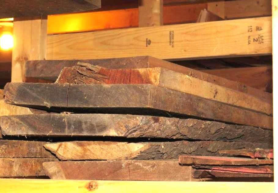 Stack of rough-cut wooden planks on a shelf, varying shades of brown.
