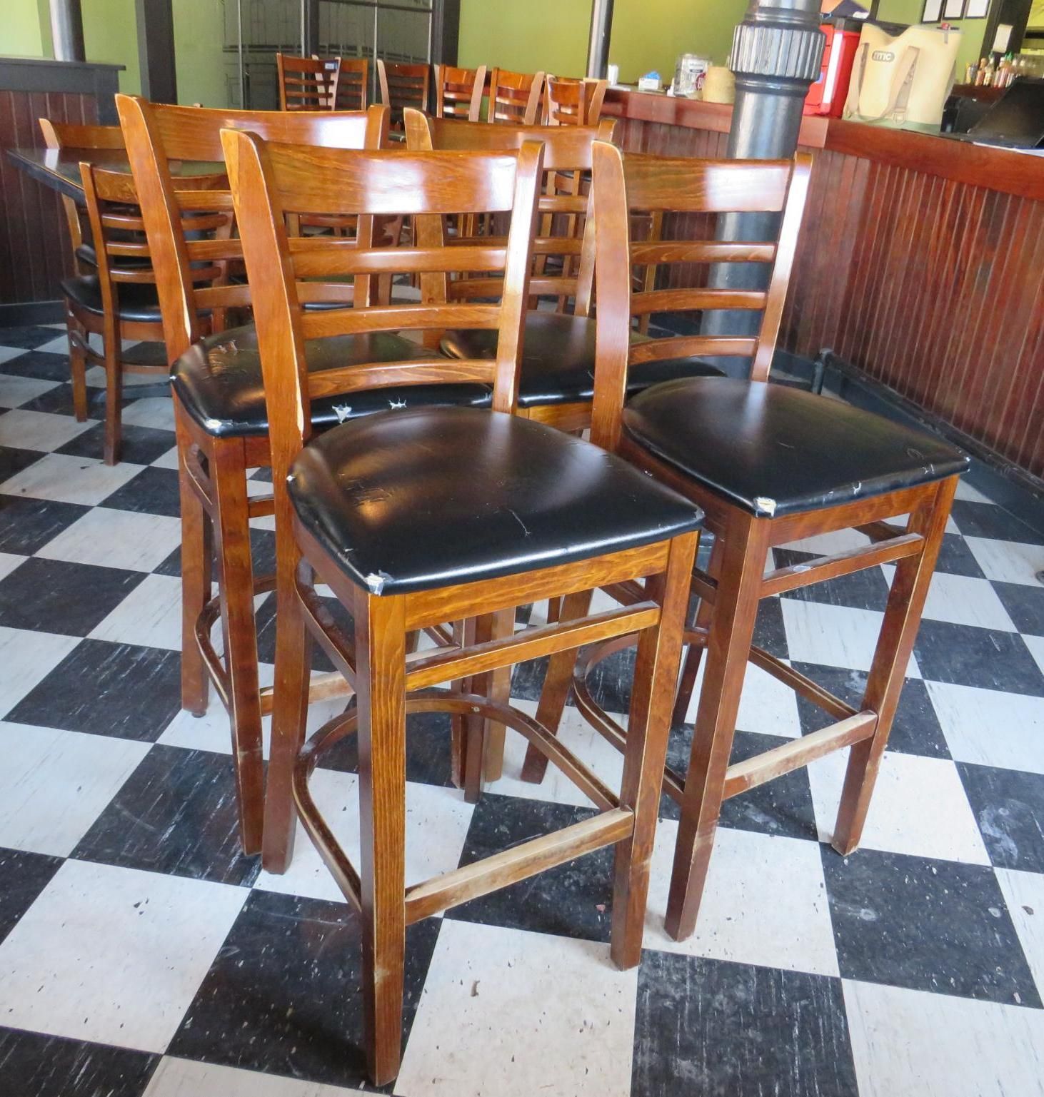 Wooden bar stools with black seats on a black and white tiled floor.