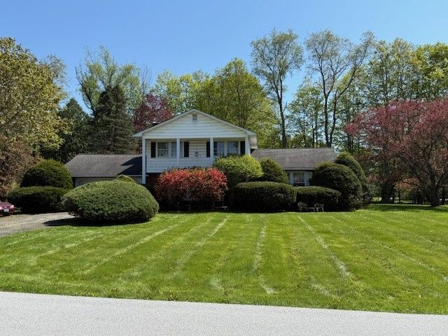 Ranch-style house with manicured lawn, shrubs, and trees under a clear blue sky.