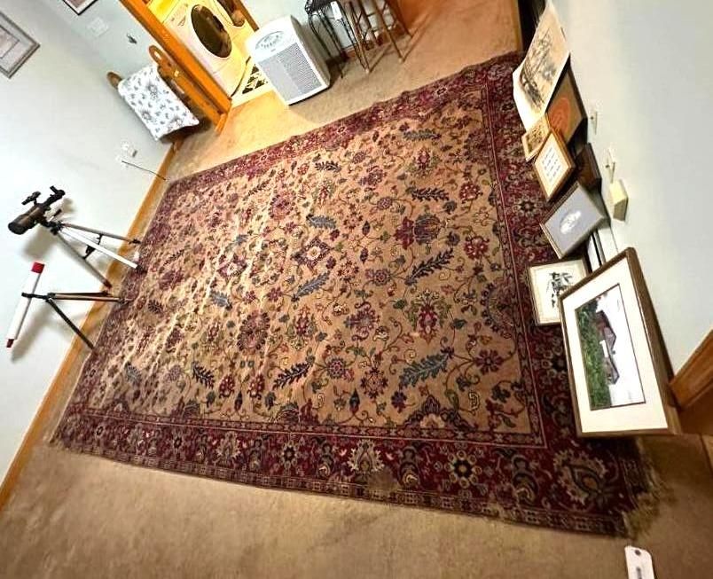 Large, ornate Persian rug with a red border and floral center on a light brown carpet.