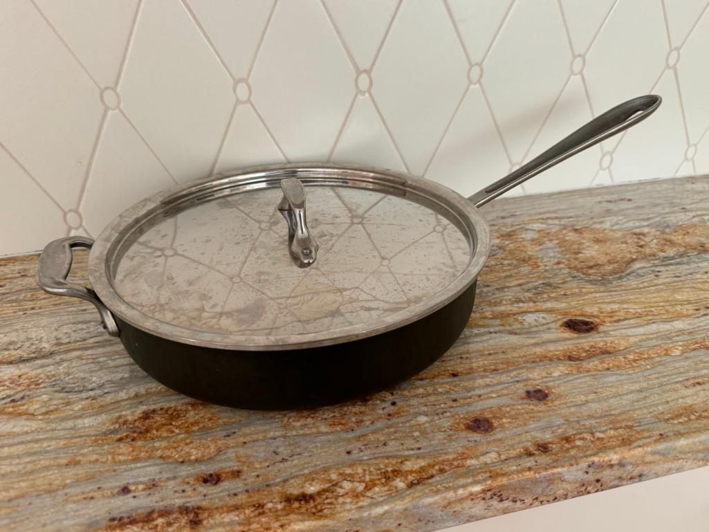 Black skillet with lid on a granite countertop, in front of a white tiled wall.