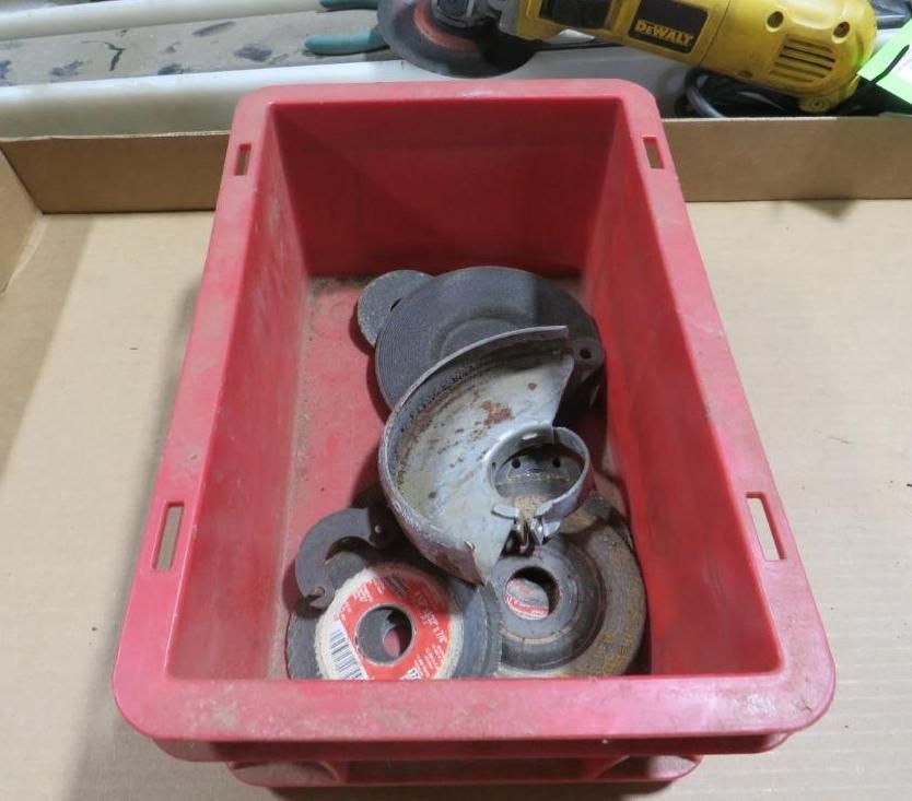 Red plastic bin containing several grinder wheels and a protective guard.