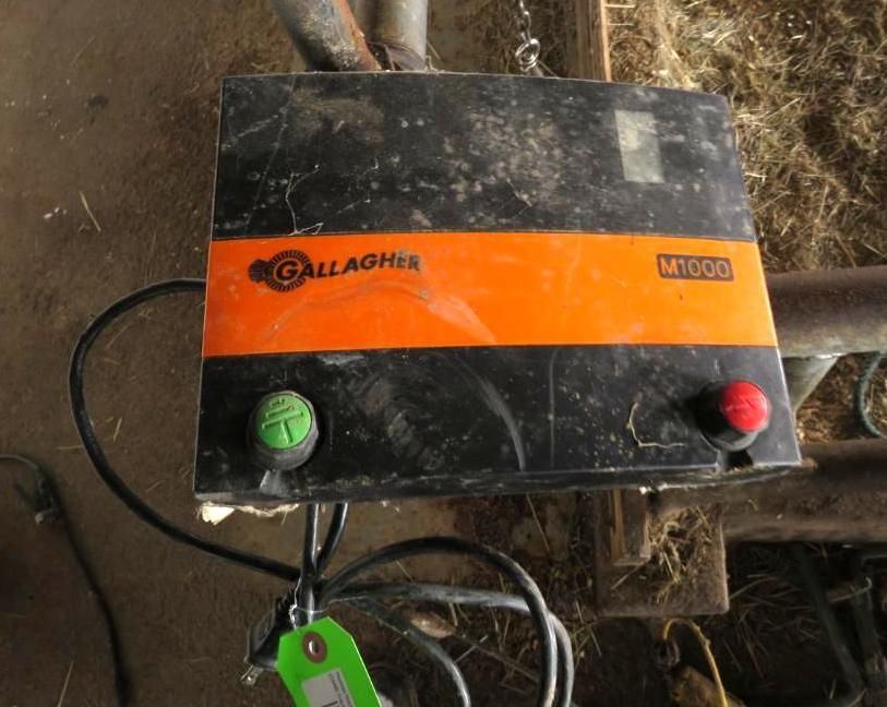 Black and orange Gallagher M1000 electric fence energizer with green and red buttons.