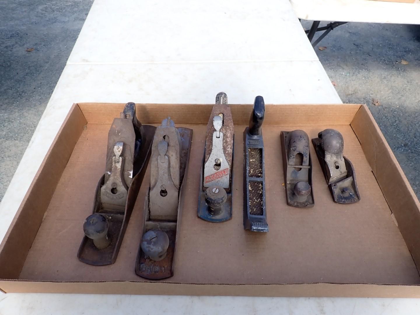 Assorted metal hand planes arranged on cardboard in a box outdoors