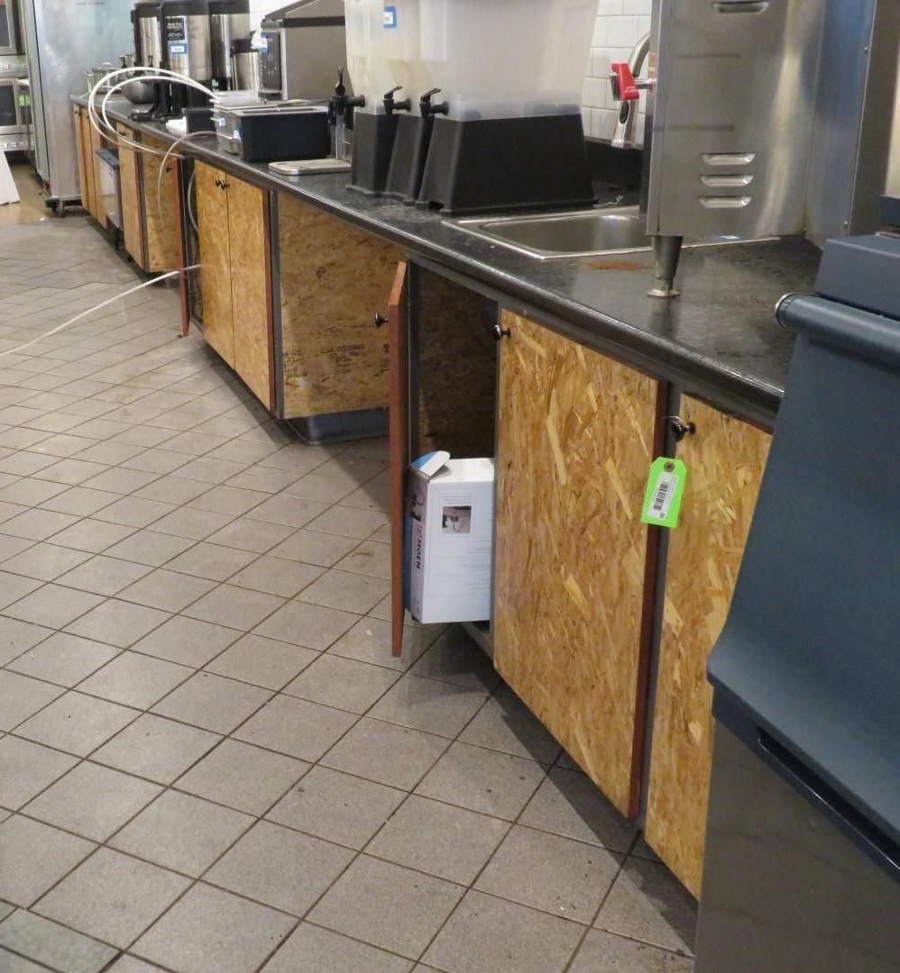 Kitchen counter with open, unfinished wood cabinets; a beverage machine and ice machine visible.